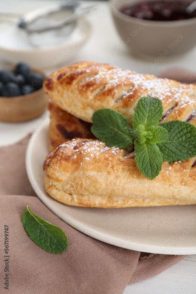 Fresh tasty puff pastry with sugar powder and mint on white table, closeup