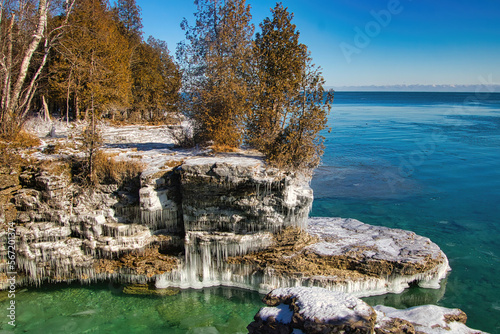 Under a blue sky on a Winter day, the rocky Lake Michigan shoreline is coated in ice at Cave Point, near Sturgeon Bay in Door Comity. photo