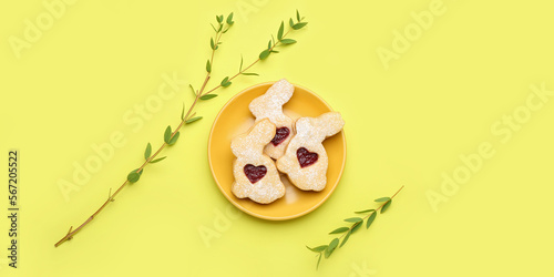 Plate with delicious Easter cookies on yellow background