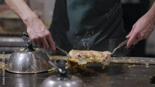This slow motion video shows the hands of a chef flipping a okonomiyaki pancake on a grill.