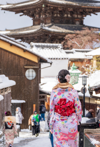 Back view of a asian young women wearing Japanese traditional kimono at Sannen-zaka street with snow in winter. Kyoto, Japan. Yasaka Pagoda in the background.