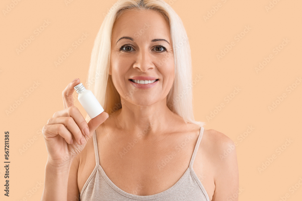 Mature blonde woman with bottle of cosmetic product on beige background Mature blonde woman with bottle of cosmetic product on beige background