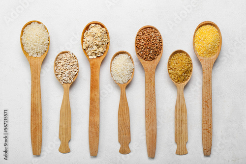 Wooden spoons of different cereals on light background