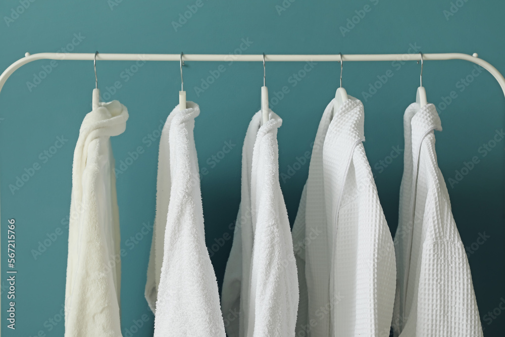 Rack with white bathrobes near color wall