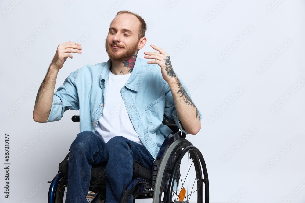 A man in a wheelchair smile, copy space, with tattoos on his arms sits on a gray studio background, the concept of health is a person with disabilities, a real person A man in a wheelchair smile, copy space, with tattoos on his arms sits on a gray studio background, the concept of health is a person with disabilities, a real person