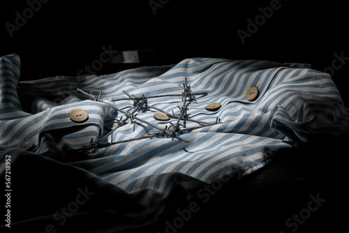 Prisoner uniform and barbed wire on dark background, closeup. International Holocaust Remembrance Day photo