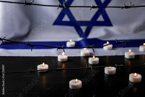 Flag of Israel, barbed wire and burning candles on black wooden table, closeup. International Holocaust Remembrance Day