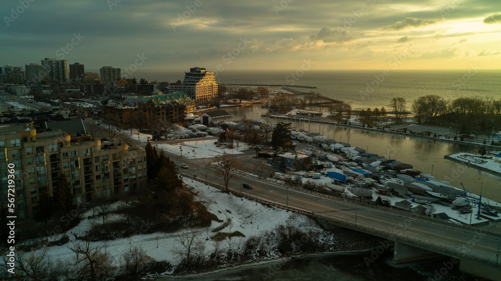 Cars on a bridge go over a frozen River as the sun rises over buildings and lake Ontario in the winter