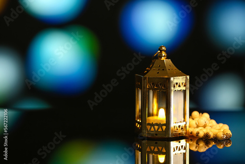 Lantern with glowing candle and prayer beads on table against blurred background. Islamic New Year celebration photo