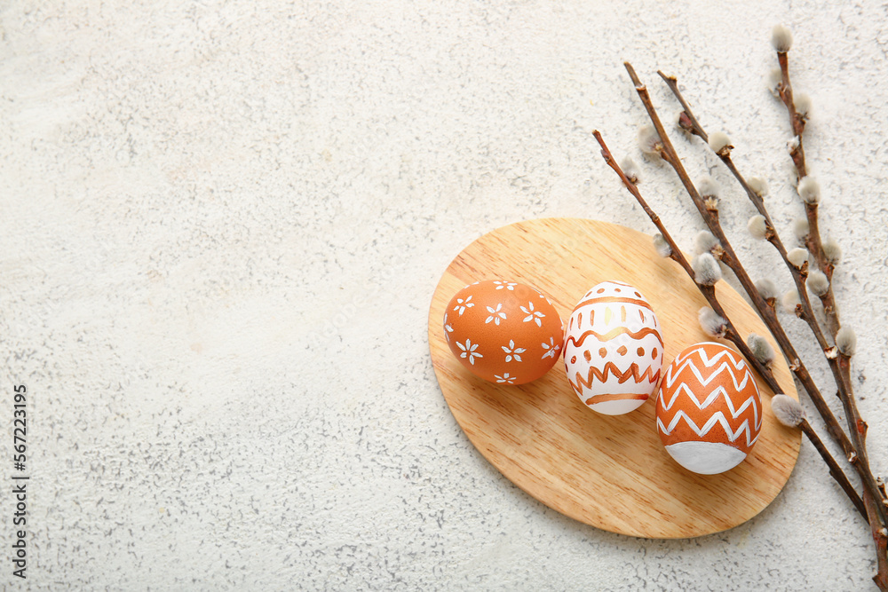 Wooden board with beautiful Easter eggs and willow branches on light background
