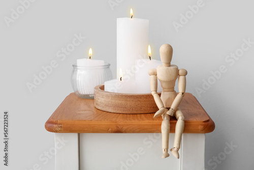 Burning candles and wooden mannequin on end table near grey wall