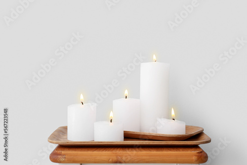 Wooden plates with burning candles on end table near grey wall