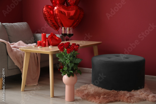 Burning candles  wine glasses and gifts for Valentine s Day on table in interior of living room