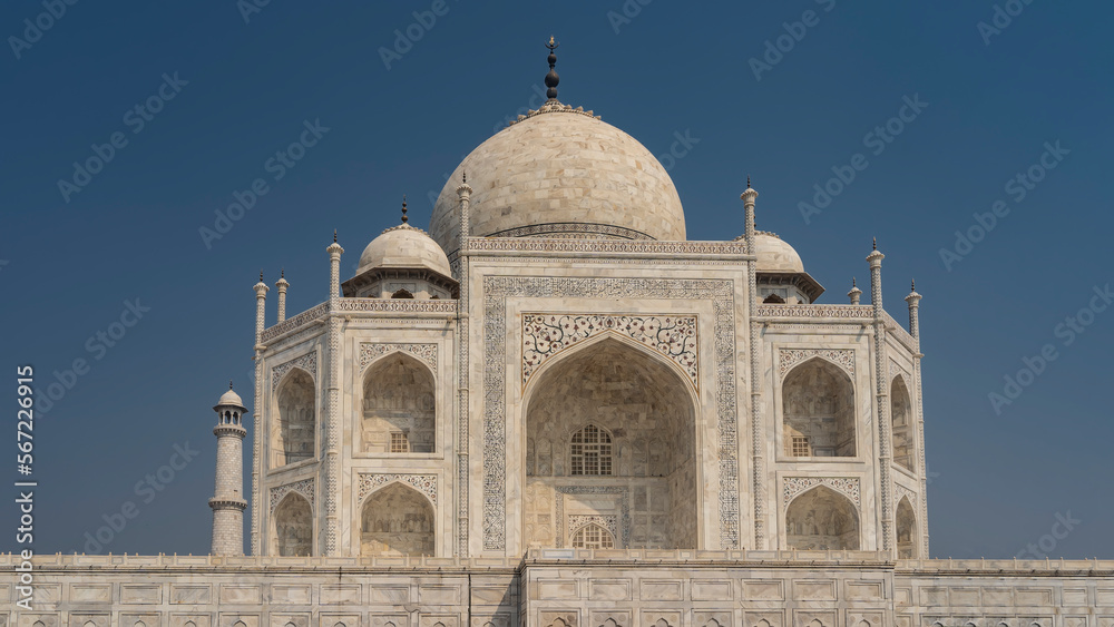 The beautiful ancient mausoleum of the Taj Mahal against the blue sky. Symmetrical white marble building with domes and minarets. Carvings and inlays of precious stones are visible on the walls. India