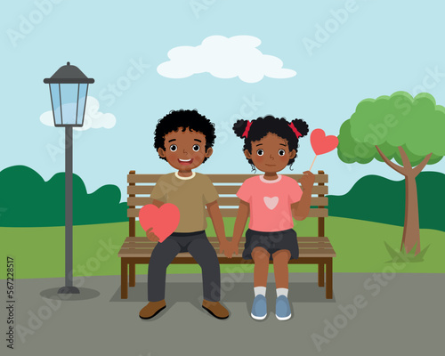 Happy valentine day little African couple boy and girl sitting on bench holding hands at the park