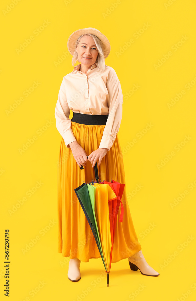 Beautiful mature woman with rainbow umbrella on yellow background