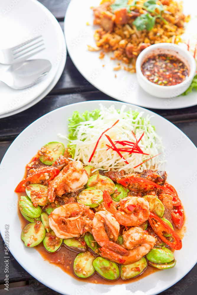 Phad Sato, stir-fried prawns with curry paste (Thai food), white plate, placed on a wooden table Phad Sato, stir-fried prawns with curry paste (Thai food), white plate, placed on a wooden table