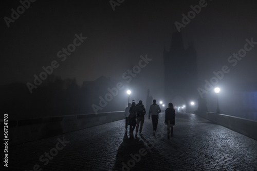 A group of young people is walking on the charles bridge in prague during night time. Scary spooky moment on a hazy and misty bridge.