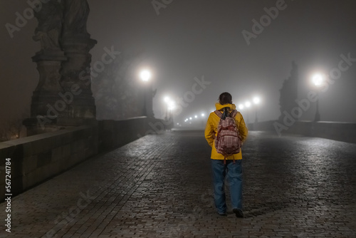 Young female is walking on an empty charles bridge in prague. Behind of a lady in bright yellow jacket and jeans walking over famous bridge.