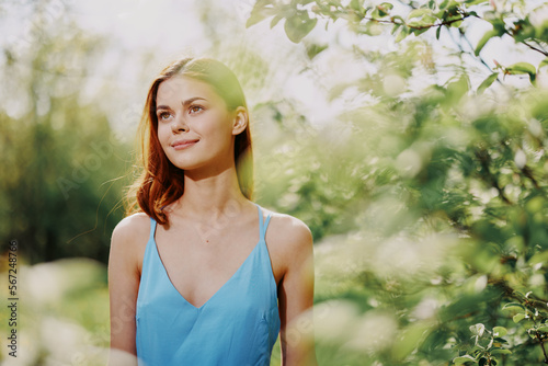 Woman smile with teeth in profile happiness in nature in the summer near a green tree in the garden of the park in a blue dress, the concept of women's health and beauty with nature sunset