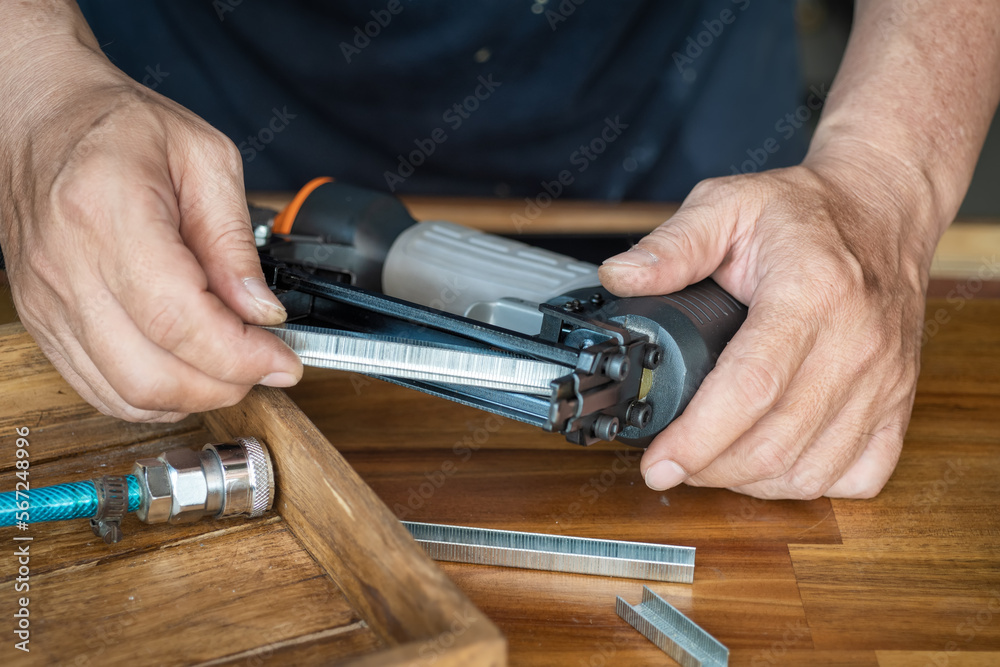 Fototapeta premium carpenter using nail gun or brad nailer tool ,load a top loading stapler in a workshop ,furniture restoration woodworking concept. selective focus