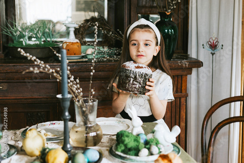 pretty little Armenian girl helps with baking for Easter on veranda on sunny spring day decorated with flowers and Easter decor, eggs, cake and willow branches, Easter family celebration