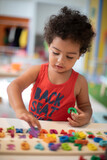 Cute toddler boy solving puzzle in a playroom with selective focus. The puzzle is with colorful alphabet and numbers.