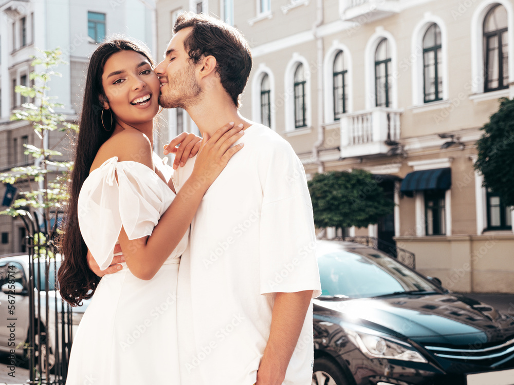 Fototapeta premium Smiling beautiful woman and her handsome boyfriend. Happy cheerful family. Sexy couple posing in the street at sunrise. During romantic date at sunny summer day outdoors. Looking at each other. Kiss