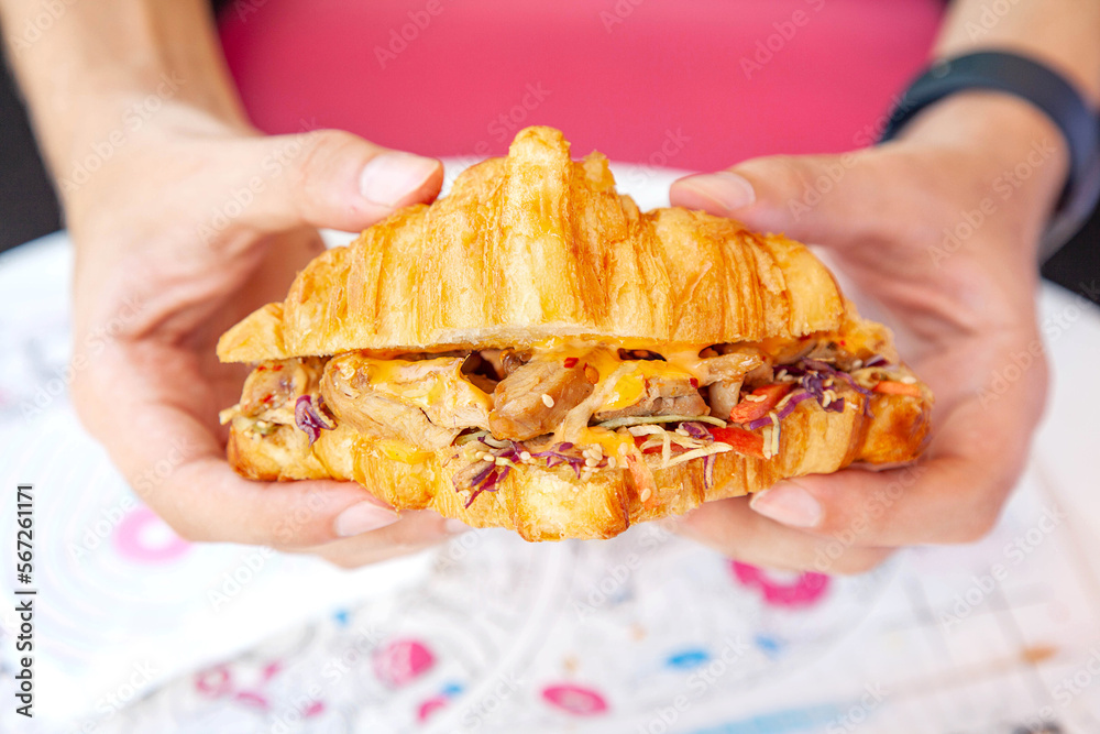 Brioche croissant grilled chicken sandwich in hand lifestyle food photography.