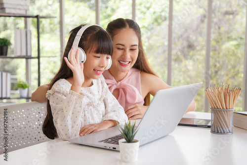 Children education and home school concept : Young asisn mother pleased to see little daughters' study online. Excited smiling child girl enjoying onlinr learning  with pleasant mom at home. photo