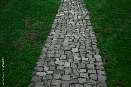 Stone block walk path. park background. pedestrian way made of gray granite paving stones in a park with green grass near a pedestrian paved path for walking in the garden, landscape, nobody.