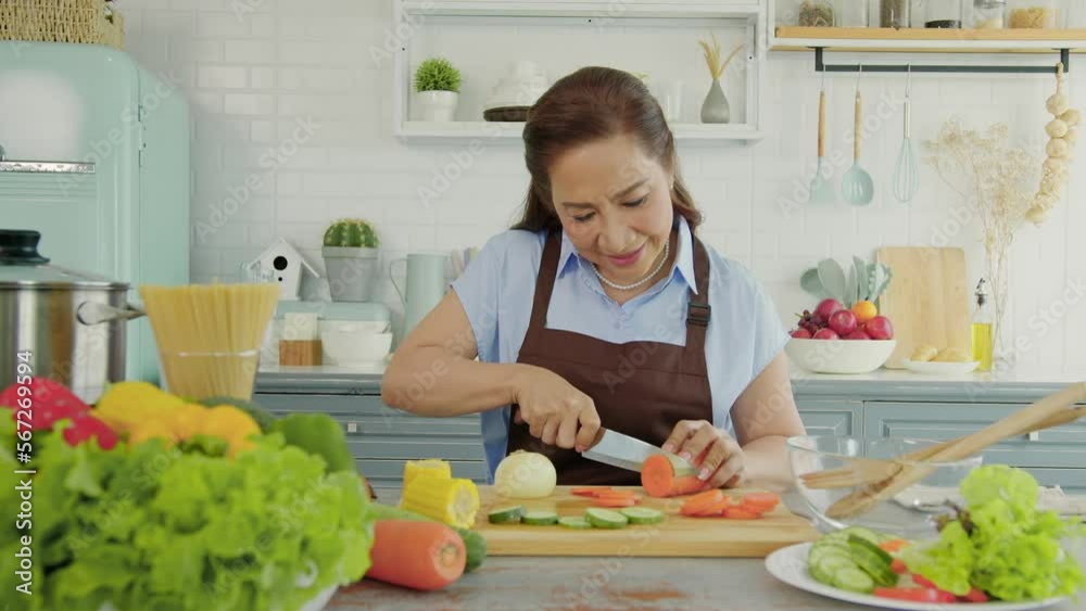 Happy smiling asian older woman in apron cut vegetables while cooking salad in kitchen. housewife cooking concept.. Happy smiling asian older woman in apron cut vegetables while cooking salad in kitchen. housewife cooking concept..