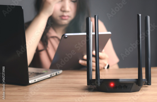 Fotótapéta Wifi router and young woman employee work from home using computer notebook and tablet videocall meeting conference angry annoy with low poor unreliable internet wifi connection problem issue outage