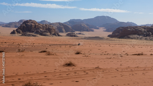 Solo four wheel drive truck driving through vast, remote wilderness of Arabian Wadi Rum desert with red sandy terrain and rugged mountainous landscape in Jordan