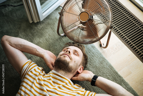 Heat wave during a summer, a man finds respite at his home balcony with the help of an electric fan. A man beats the summer heat wave by finding relief with an fan. The effect of global warming photo