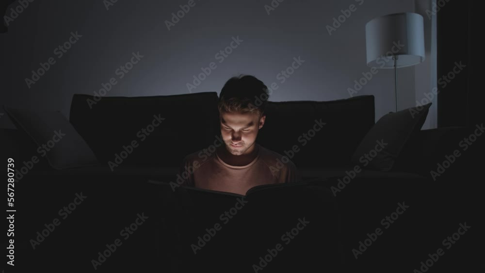 Night time, young man sitting at living room on the floor and reading a book, warm light, man in a self-isolation. Night time, young man sitting at living room on the floor and reading a book, warm light, man in a self-isolation.