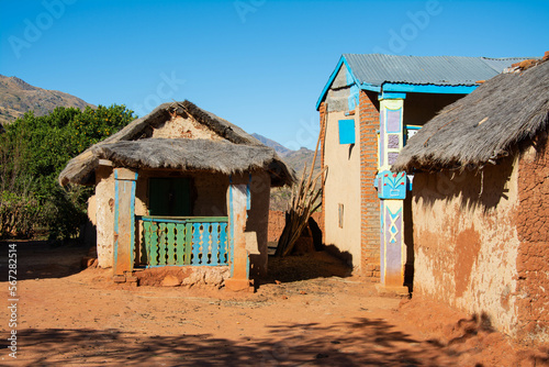 Malagasy village in Madagascar.
Three orange brick cottages with thatched roofs with blue sky in the background. Poor African village. Poor Madagascar houses. photo