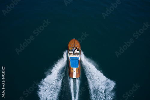 Luxurious wooden big boat with people moving fast on dark water top view. Couple man and woman luxury boat on the water top view.