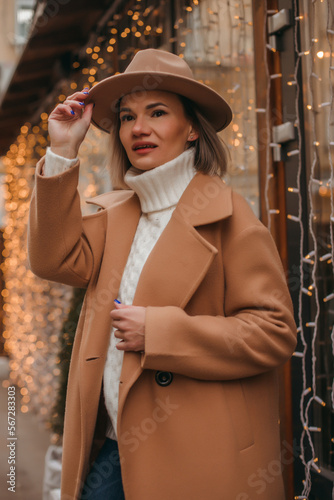 Outdoor fashion portrait of an elegant woman in a beige hat and coat posing in a european city.