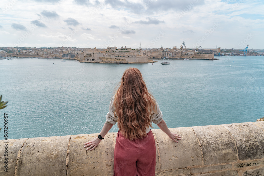 woman standin at a wall looking at a panoramic view of the three cities in valletta