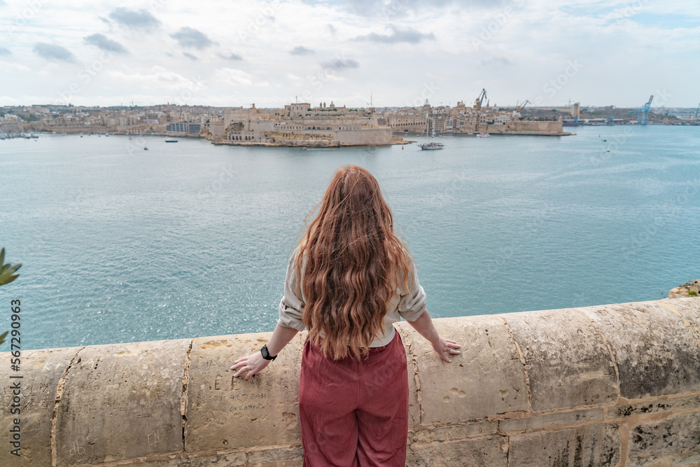 woman standin at a wall looking at a panoramic view of the three cities in valletta