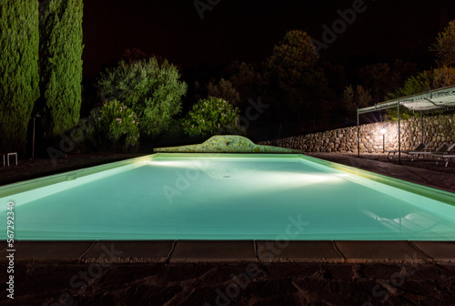 Illuminated swimming pool on the Montemassi hillside surrounded by cypresses and oleanders n the province of Grosseto. Italy