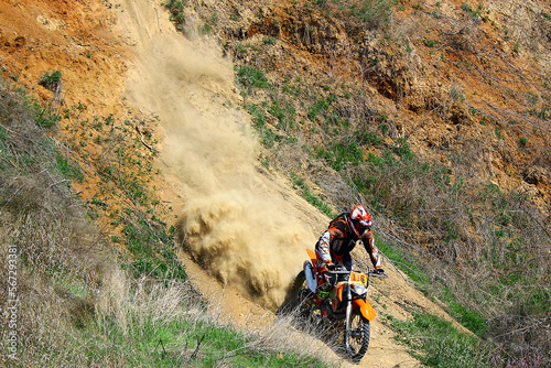 A motorcyclist on an enduro motorcycle descends a mountain with a lot of dust 