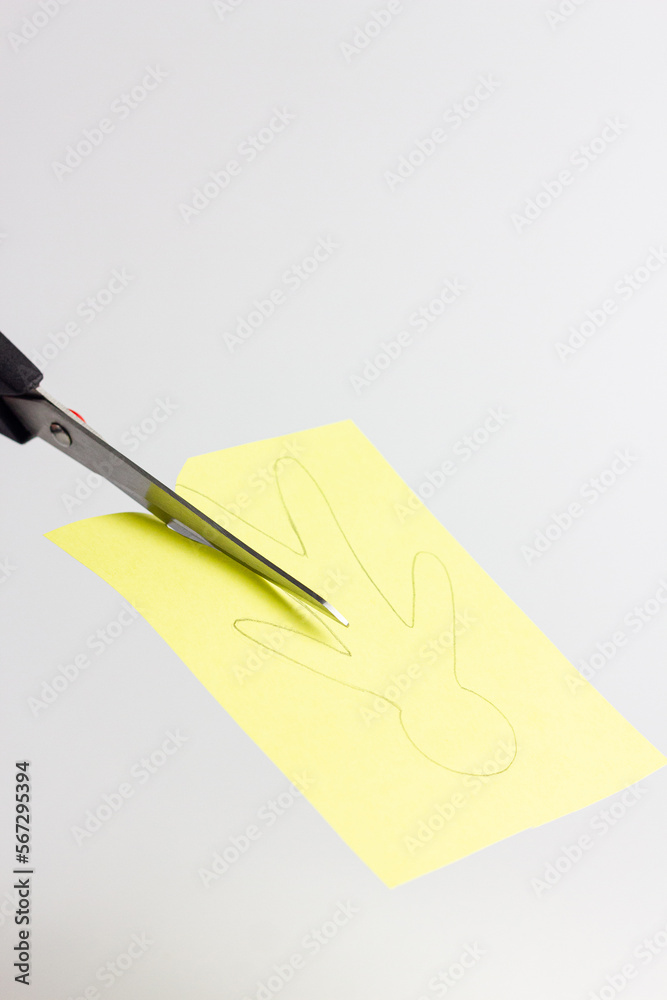 Steel scissors on a white background cut a silhouette of a person from yellow colored paper. Paper application. Metal scissors with black handles. Horizontal format. Handmade, craft, work with paper. Steel scissors on a white background cut a silhouette of a person from yellow colored paper. Paper application. Metal scissors with black handles. Horizontal format. Handmade, craft, work with paper.