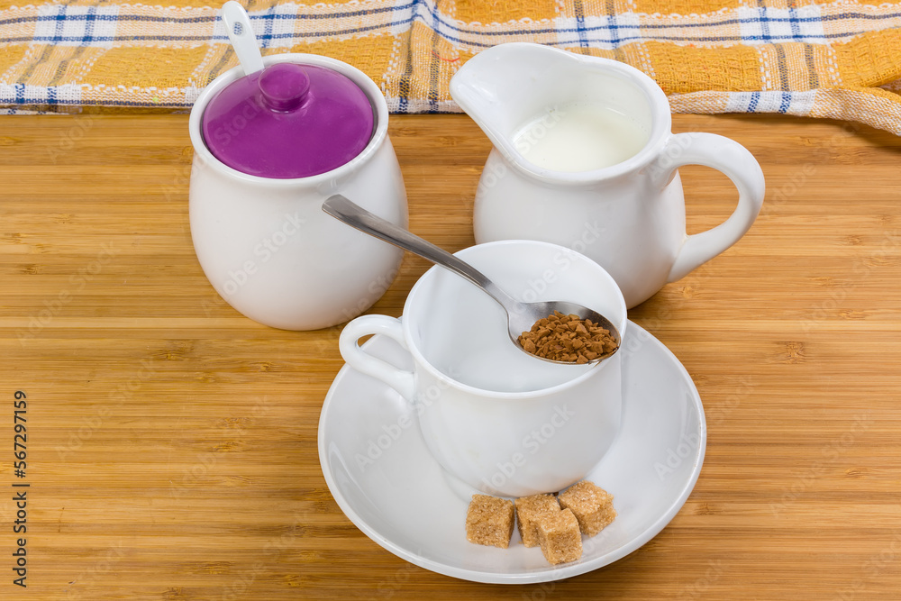 Fototapeta premium Instant coffee granules in spoon atop empty cup, milk, sugar