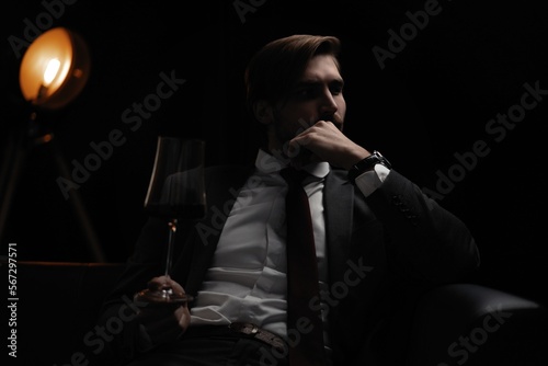 Portrait of handsome elegant man with a glass of wine in a dark room