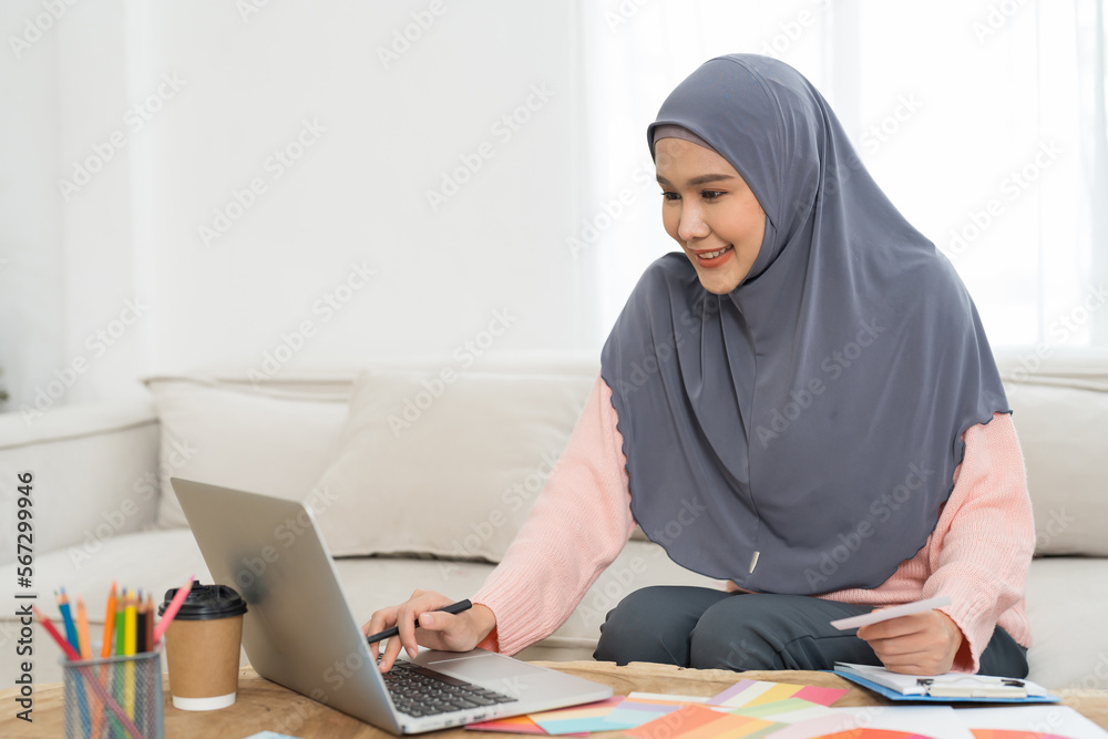 Asian young Muslim woman graphic designer wear hijab headscarf working and design color swatches samples with laptop computer in the workshop. Interior design and renovation concept