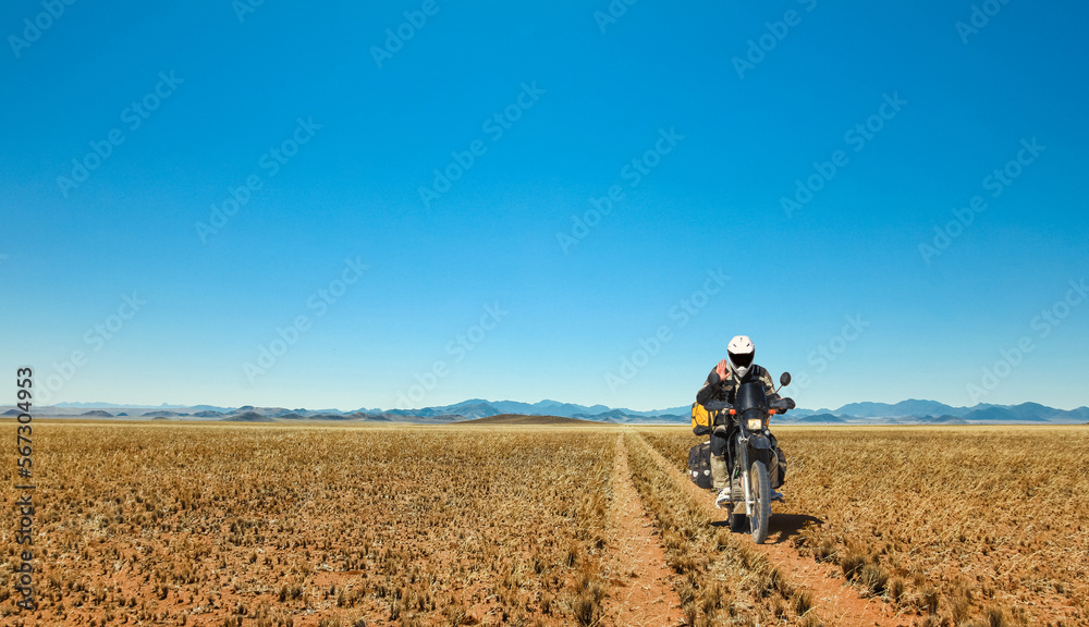 One Motorbiker driving on dirt road through grasland desert. Motorcycle Adventure in Namib, Namibia.