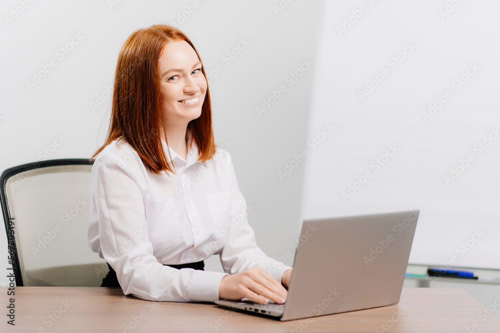 a red-haired woman works at the computer in an office with white walls. a red-haired woman works at the computer in an office with white walls.