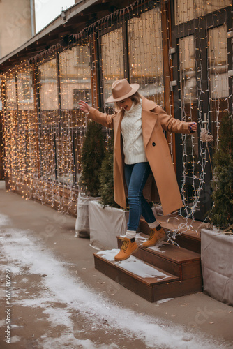 Outdoor fashion portrait of an elegant woman in a beige hat and coat posing in a european city.